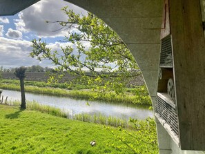 A view through an archway of a river, grassy banks, and a tree with green leaves. - 5 Pers Holiday Home Horizon Close to the National Park Lauwersmeer (Anjum)