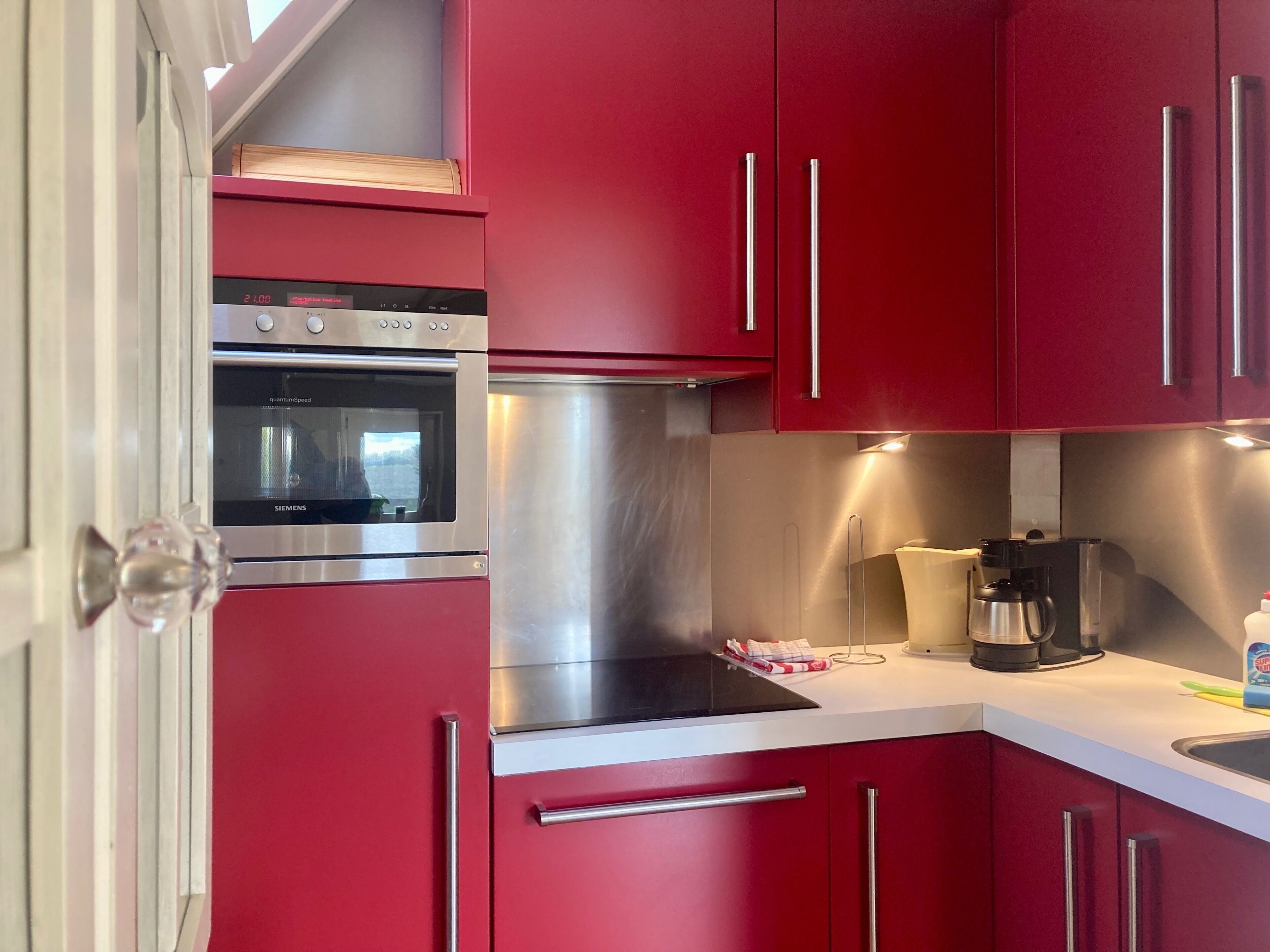 Una cocina con gabinetes rojos, un horno de acero inoxidable y una cafetera.