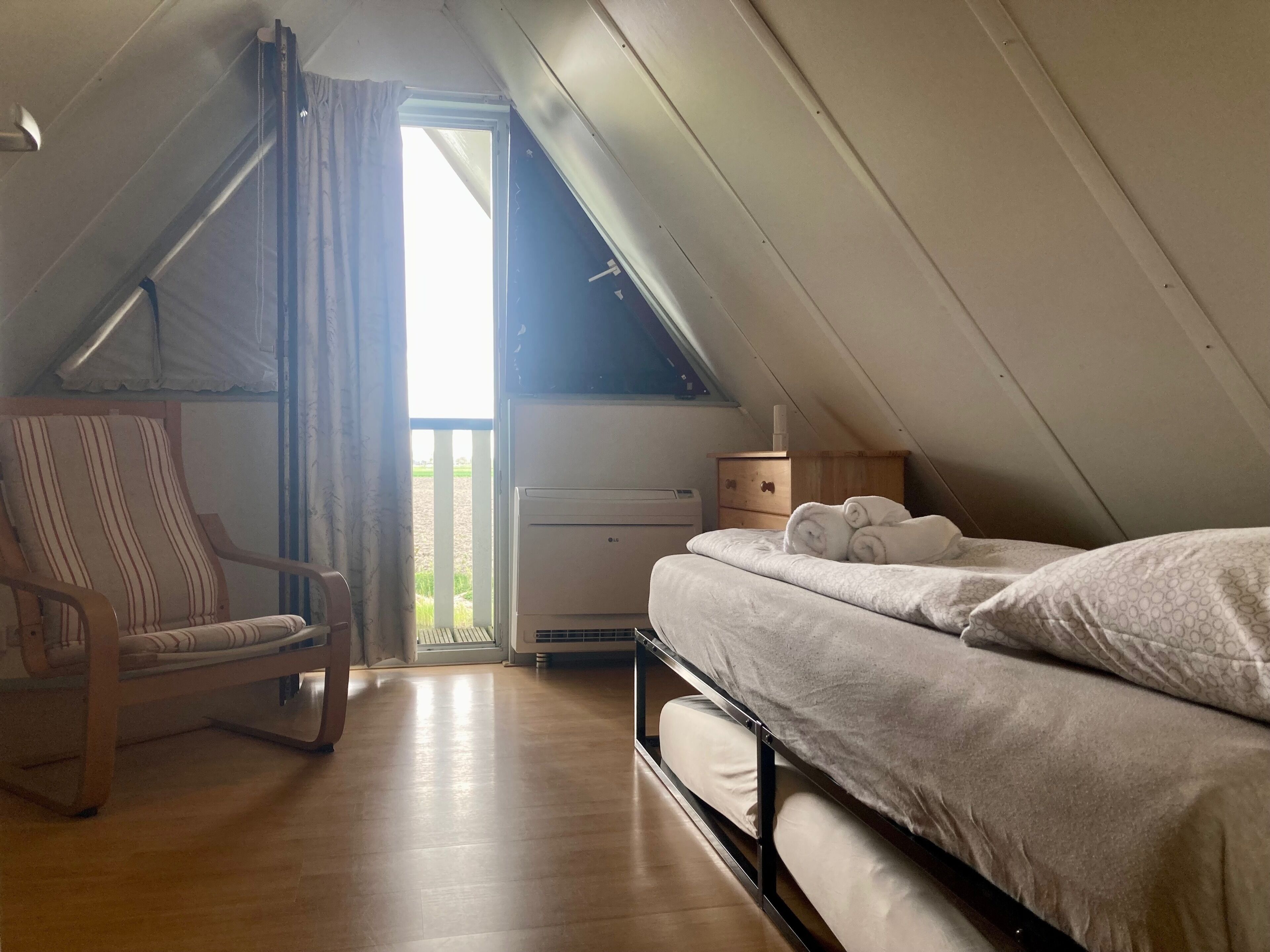 A bedroom with a bunk bed, a wooden chair, a bedside table with a lamp, and a window with curtains.