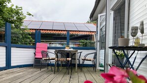 A wooden deck with a table and chairs, a potted plant, and a closed shutter door. - Beautiful Quiet 2 Persons Caravan on the Lauwersmeer (Anjum)