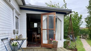 A wooden deck with a sliding glass door leading to a room with a chair and a small table. - Beautiful Quiet 2 Persons Caravan on the Lauwersmeer (Anjum)