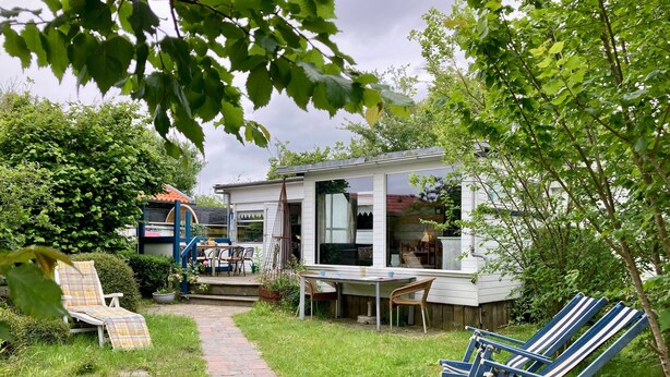 A house with a patio, outdoor seating, and a garden. - Beautiful Quiet 2 Persons Caravan on the Lauwersmeer (Anjum)