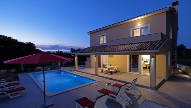Una casa de dos pisos con piscina, mobiliario exterior y un patio cubierto.