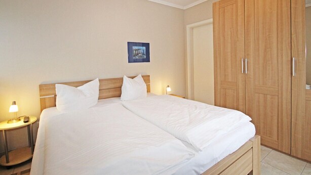 Una camera d'albergo con un letto grande, due comodini con lampade, un armadio in legno e un quadro appeso al muro.