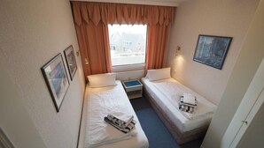 A small hotel room with two single beds, a window with curtains, a framed picture on the wall, and a small table. - Appartement 163 (Sylt)