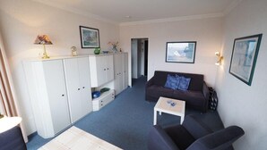 A living room with a sofa, a coffee table, a cabinet, and a framed picture on the wall. - Appartement 163 (Sylt)