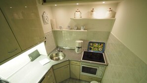 A compact kitchen with a sink, stove, and microwave. There are shelves above the counter holding jars and a coffee maker. - Appartement 163 (Sylt)