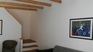 A living room with a grey sofa, a coffee table with magazines, a wooden staircase, and a framed abstract painting on the wall. - Ferienhaus Jana (Wernigerode)