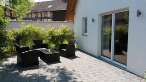 An outdoor patio with a seating area, a sliding glass door, and a view of a traditional building in the background. - Ferienhaus Jana (Wernigerode)