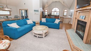 A spacious living room with two blue sofas, a round coffee table, and a fireplace. - Oceanside, Hot Tub, Close to Beach, Sunroom, CP7, Shoulda Been Here Yesterday (Corolla)