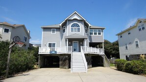 A two-story house with a front porch, a basketball hoop, and a staircase leading to a second-floor balcony. - Oceanside, Hot Tub, Close to Beach, Sunroom, CP7, Shoulda Been Here Yesterday (Corolla)