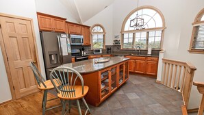A spacious kitchen with wooden cabinets, a large island, and a view through arched windows. - Oceanside, Hot Tub, Close to Beach, Sunroom, CP7, Shoulda Been Here Yesterday (Corolla)