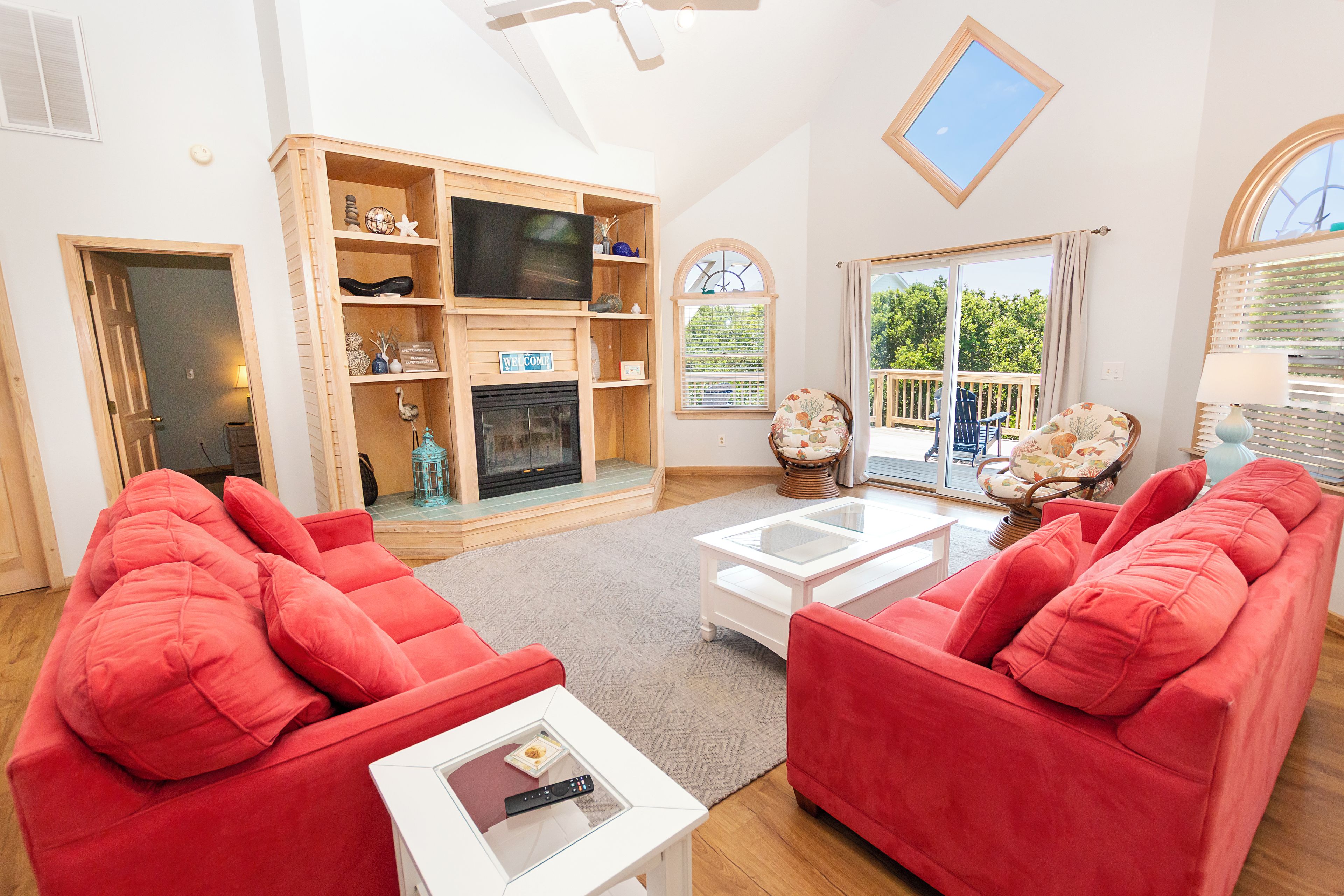 Un salon avec des canapés rouges, un téléviseur à écran plat, une cheminée et un balcon aménagé avec du mobilier d’extérieur.