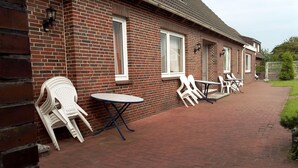 A brick building with a patio area featuring white plastic chairs and tables. - Nordsee-ferienanlage -wohnung Langeoog- (Dornum)