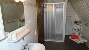 Une salle de bain équipée d’une douche, de toilettes, d’un lavabo et d’une petite table sur laquelle est posée une serviette rouge.