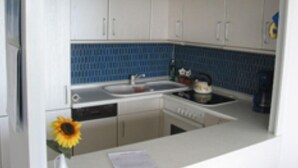 A small kitchen with white cabinets, a blue backsplash, a sink, and a stove. - Ferienwohnung im Wikingturm (Schleswig)