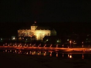 Un edificio grande e iluminado de noche, con un puente largo en primer plano.
