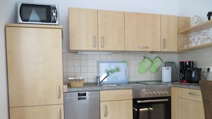 A compact kitchen with wooden cabinets, a dishwasher, a stove, and a microwave. - Weißes Haus am Kurpark, Fewo Waldblick (Quedlinburg)