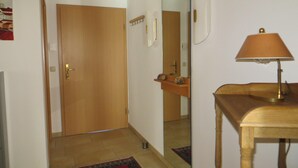 A hallway with a wooden door, a mirror, a small table with a lamp, and a rug on the floor. - Weißes Haus am Kurpark, Fewo Waldblick (Quedlinburg)