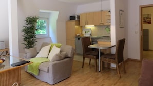 A compact living space with a sofa, dining table, chairs, a kitchen area, and a potted plant. - Weißes Haus am Kurpark, Fewo Waldblick (Quedlinburg)