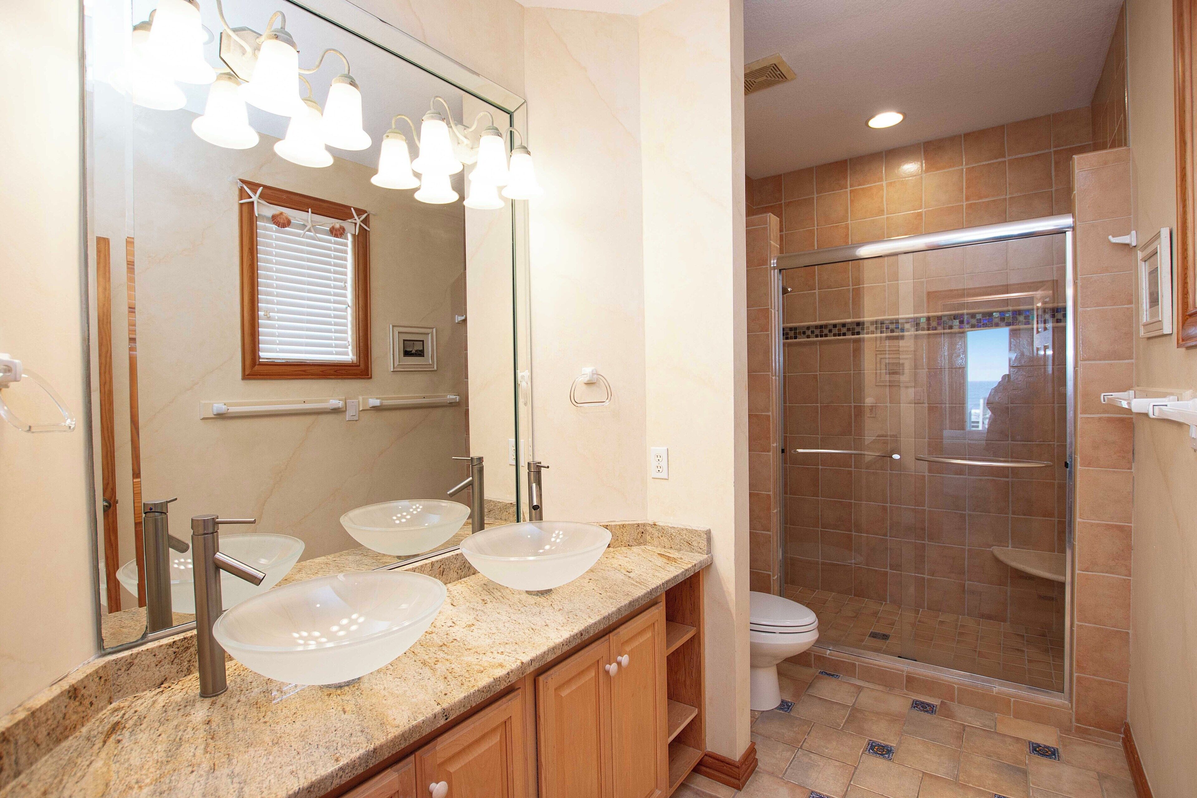 A bathroom with a large mirror, two vessel sinks, a shower enclosure, and a toilet.