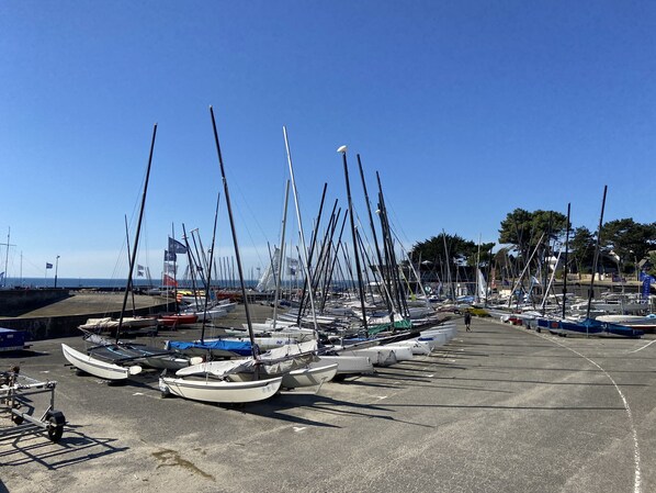 Un port de plaisance où sont amarrés de nombreux voiliers, sur une zone en béton, entouré d’arbres et sous un ciel bleu dégagé.
