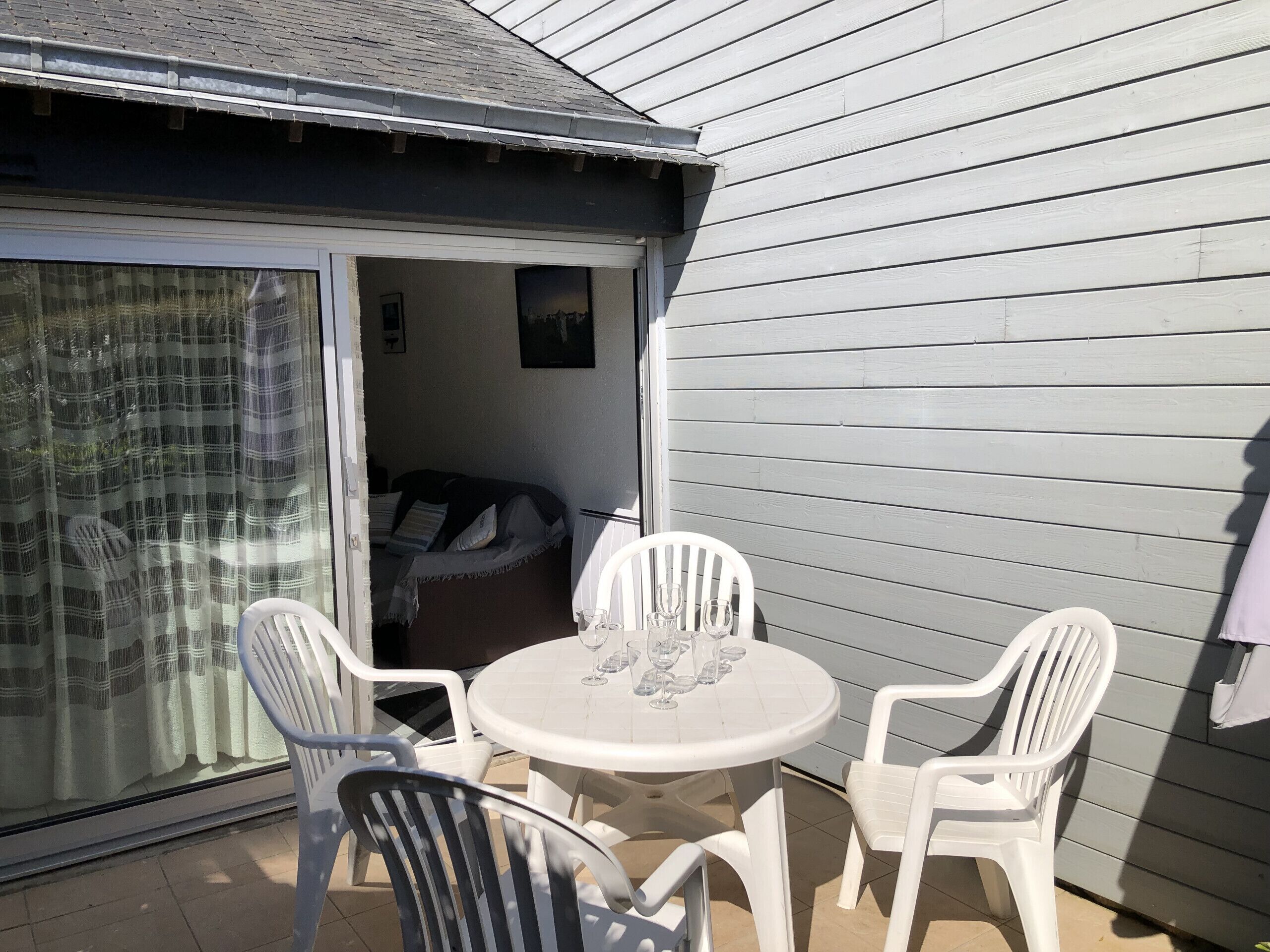 A patio with a round table and four chairs, a sliding glass door leading to a room, and a grey exterior wall.