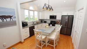 Una cocina moderna con armarios blancos, un refrigerador de acero inoxidable, un microondas y un lavavajillas. Hay un ventanal que proporciona luz natural y vistas al exterior.