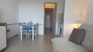 A compact living space with a kitchenette, a dining area with a table and chairs, and a patterned sofa.