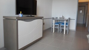 A small kitchenette with a flat-screen TV, a microwave, and a small refrigerator. There is a dining area with a table and chairs.