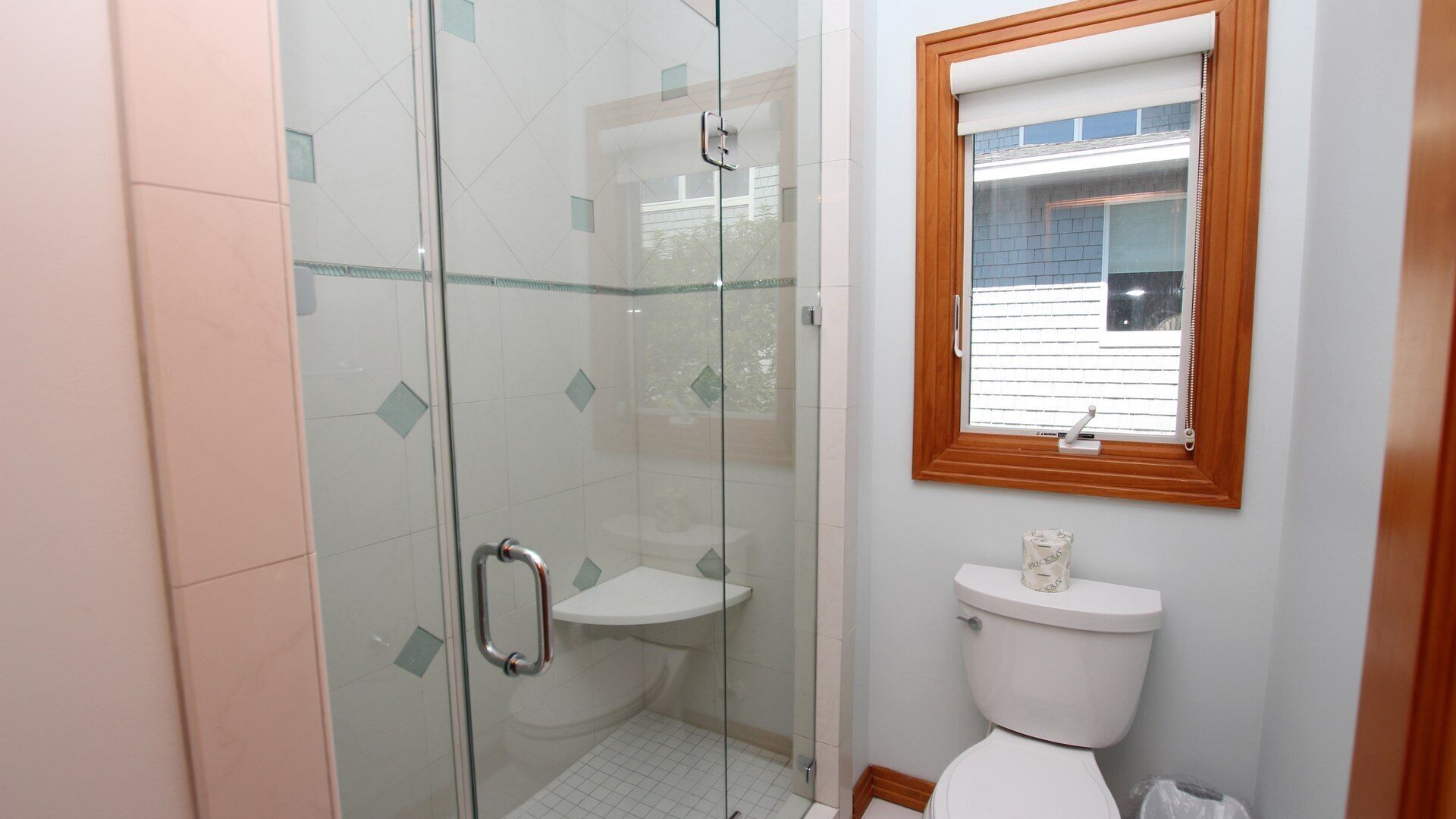 Un baño con ducha compartimentada por vidrio, un inodoro y un ventanal con marco de madera.