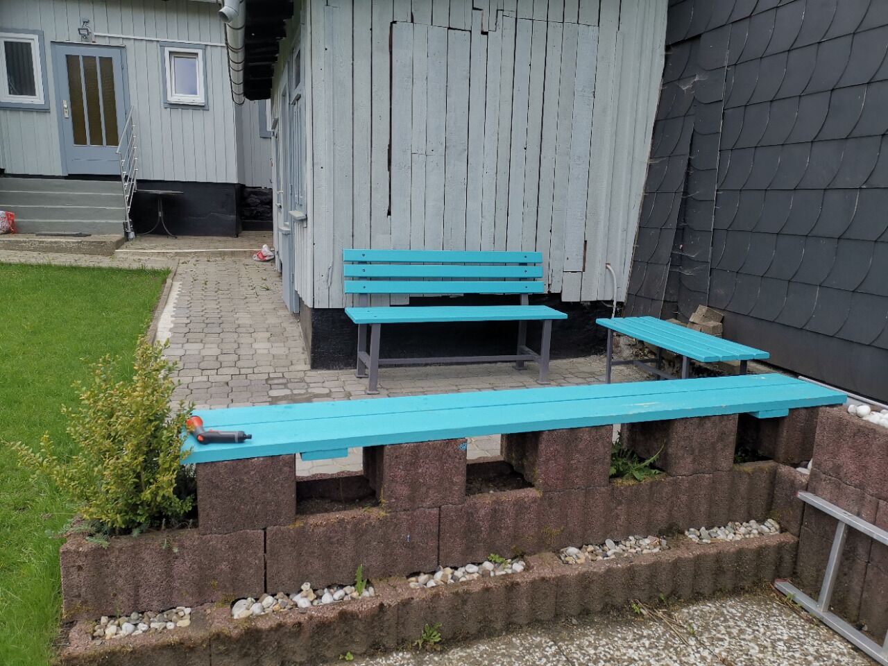 A patio area with two turquoise benches and a small table, surrounded by a brick wall and a grassy lawn.