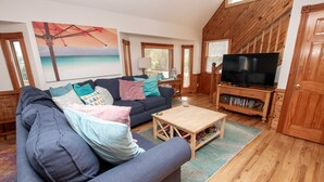 A cozy living room with a sofa, a coffee table, and a TV on a wooden stand. - Oceanside, Private Pool, Screened Porch, Hot Tub! WW910, Serenity on the Beach (Corolla)