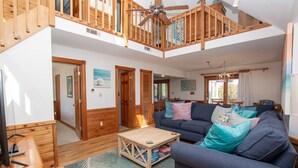 A spacious living area with a high ceiling, wooden staircase, and a large sofa with multiple cushions. - Oceanside, Private Pool, Screened Porch, Hot Tub! WW910, Serenity on the Beach (Corolla)