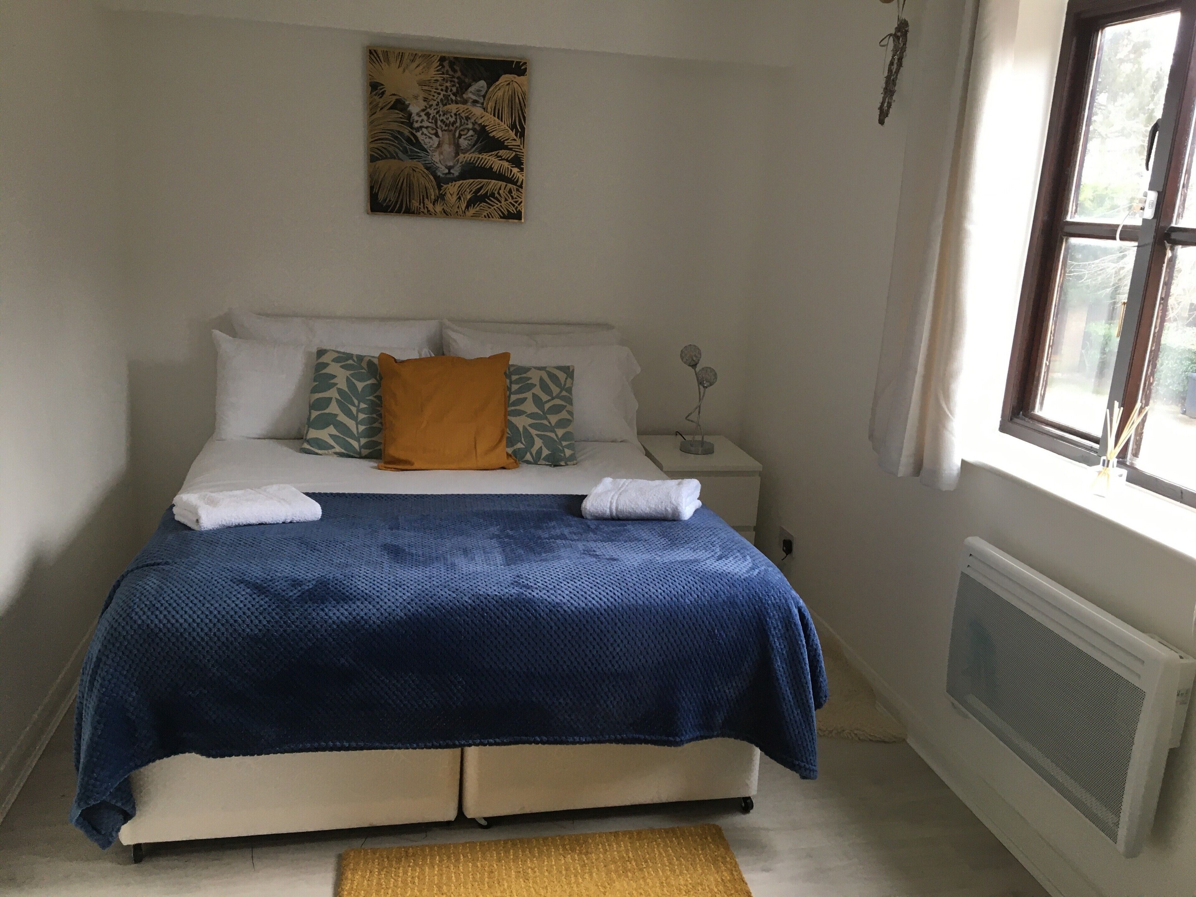 A bedroom with a bed, pillows, a nightstand, a window, and a radiator.