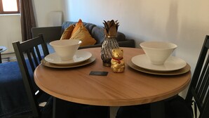 A round wooden table with two white bowls on plates, a small golden teddy bear, and a decorative vase with leaves.