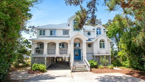 A two-story house with a front porch, a blue door, and a small garden area. - Soundfront, Amazing Sound Views! Sunsets, Yard, Hot Tub, MS100, Timberly II (Corolla)