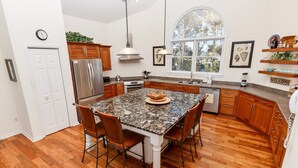 A modern kitchen with a granite island, wooden cabinets, stainless steel appliances, and a large window providing natural light.