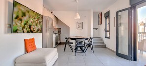 Um apartamento moderno com área de refeições, cozinha e um sofá com almofada laranja.