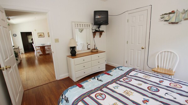 A bedroom with a bed, dresser, TV, and a chair.
