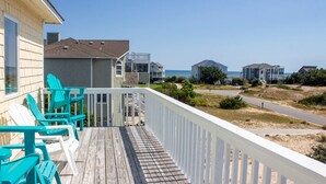 A wooden deck with turquoise chairs, a white railing, and a view of beachfront buildings. - Walk to Beach, Lighthouse & Historic Corolla, Near Corolla Adventure Park, Pool & Hot Tub (Corolla)