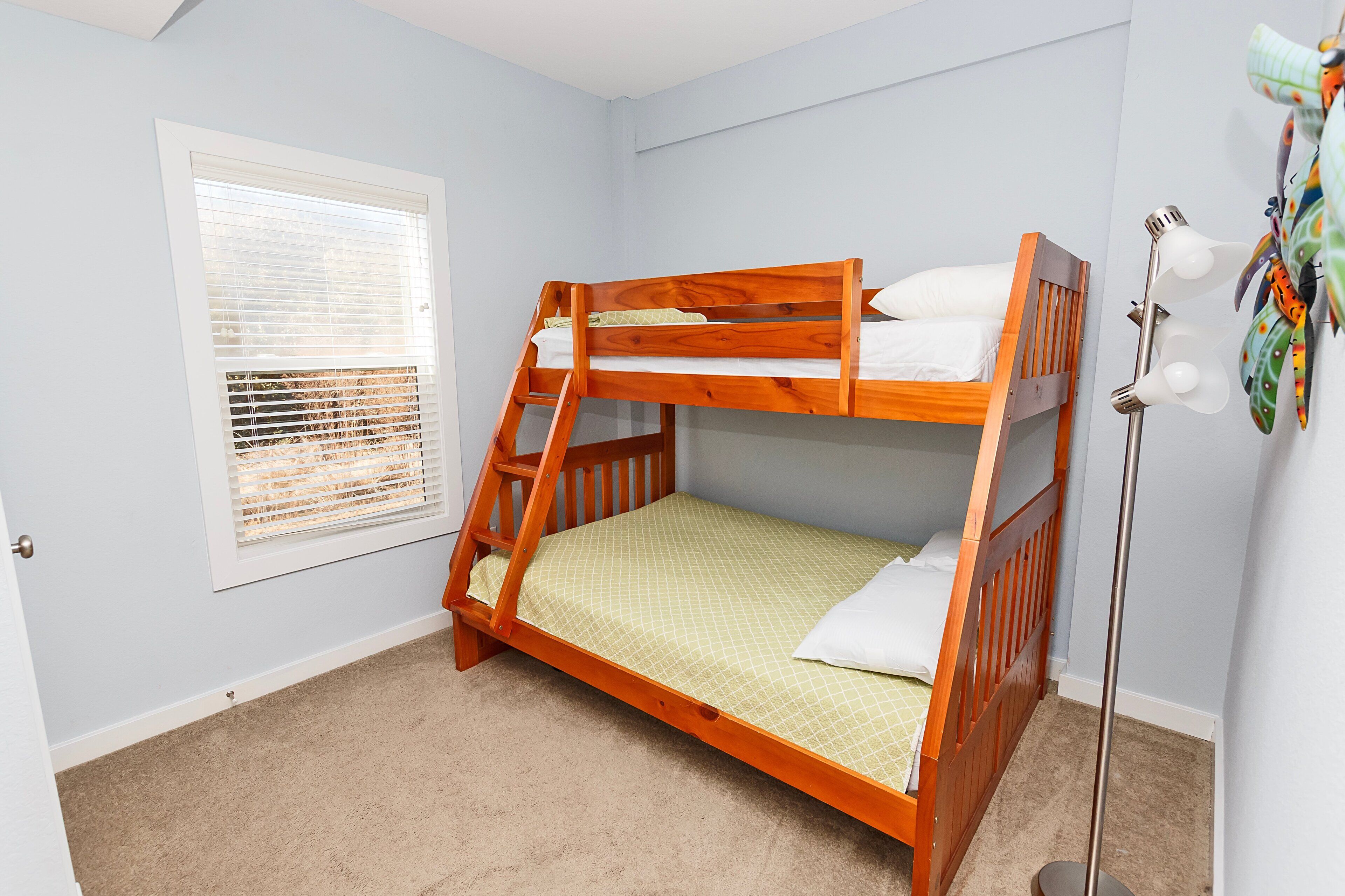 A bunk bed in a room with a window and a floor lamp.