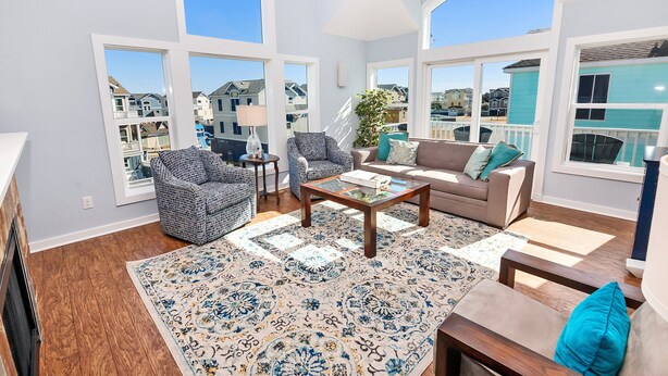 A spacious living room with a large window, a ceiling fan, and a view of neighboring houses. - Moms Dream- Oceanside, Comm Pool, Hot Tub, Yard, CB10, Dads Mercedes (Corolla)