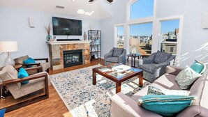 A spacious living room with a fireplace, comfortable seating, a flat-screen TV, and large windows offering a view of the neighborhood. - Moms Dream- Oceanside, Comm Pool, Hot Tub, Yard, CB10, Dads Mercedes (Corolla)