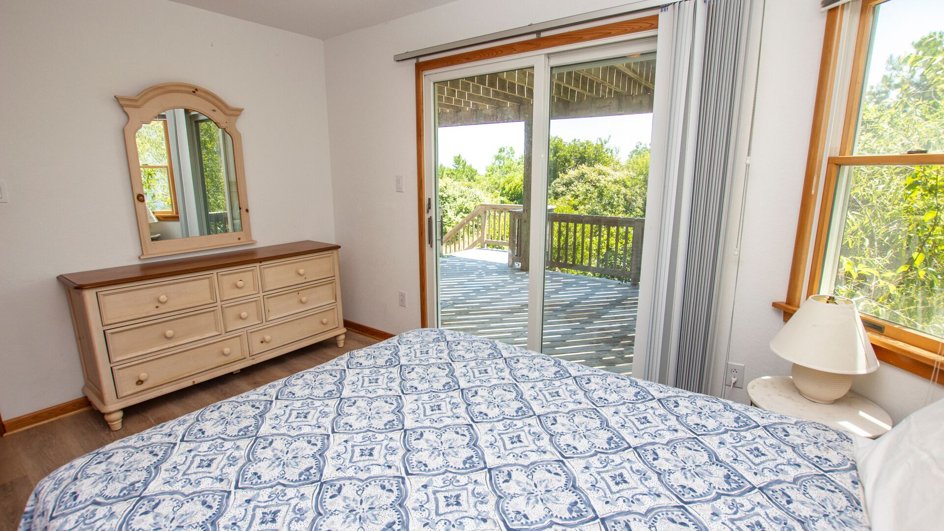 Un dormitorio con cama, cómoda, espejo y vistas a un balcón con mobiliario exterior.