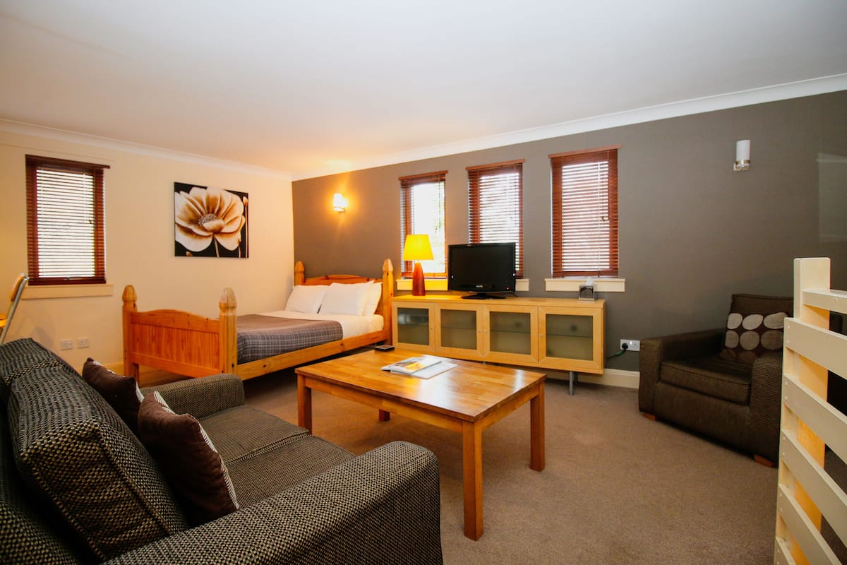 Um quarto acolhedor com cama, sofá e uma pequena TV sobre um móvel de madeira.