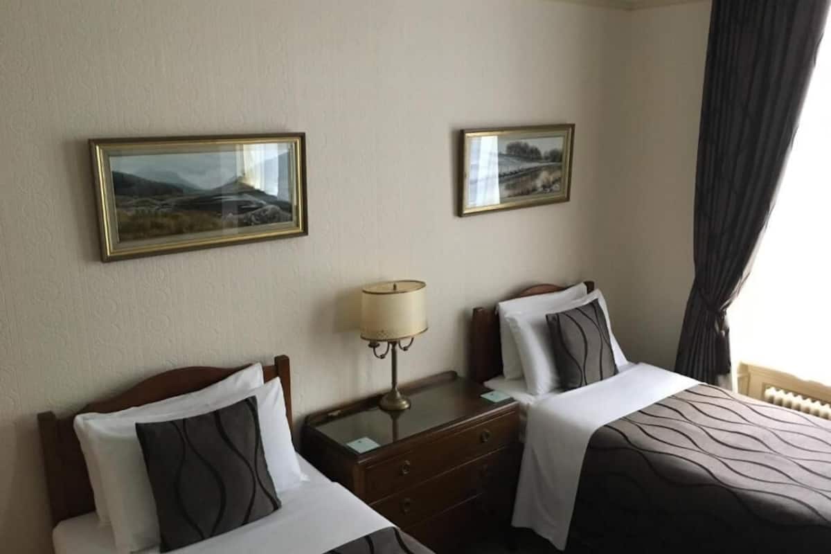 Quarto de hotel com duas camas, uma mesa de cabeceira com abajur, e duas imagens emolduradas na parede.