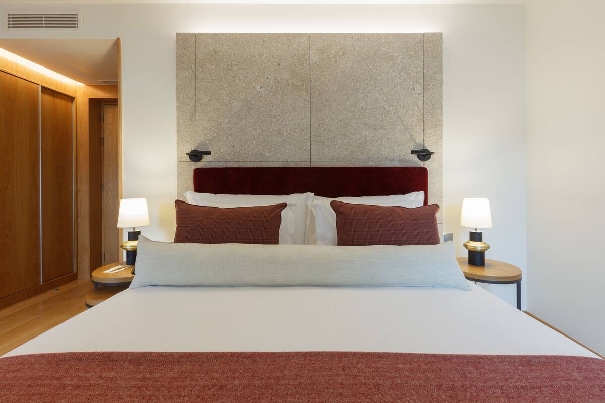 A hotel room with a large bed, two bedside lamps, a wooden wardrobe, and a stone accent wall.
