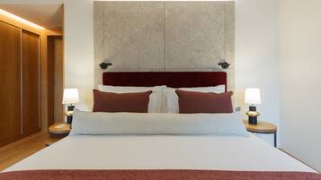 A hotel room with a large bed, two bedside lamps, a wooden wardrobe, and a stone accent wall.