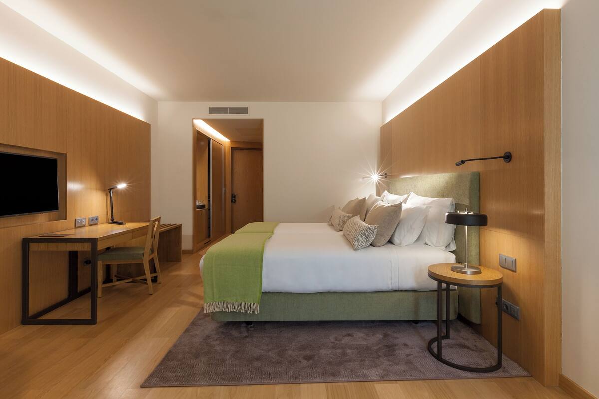A modern bedroom with a bed, bedside table, lamp, and a desk with a chair.